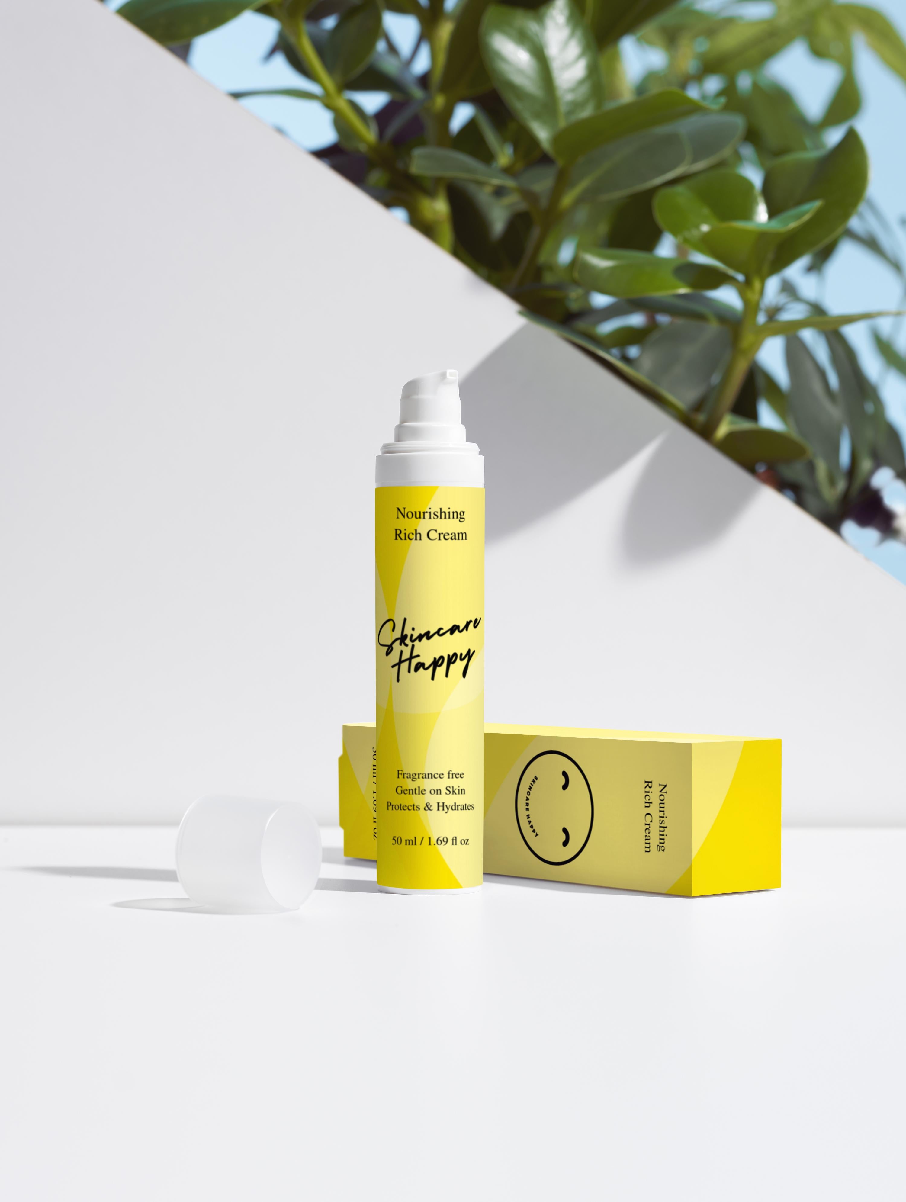 Skincare product with yellow packaging and white cap on a white surface with green leaves in the background